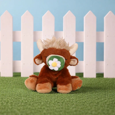 Binky Cow - Gus by Dinkum Pets is a soft brown Highland cow plush with horns and a flower binky sitting on grass by a white fence