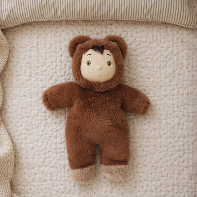 Cozy Day Dinkum - Bobby Bear soft doll in a brown bear suit lying on a quilted blanket. A cuddly toy for imaginative play by Cozy Dinkums