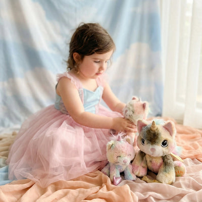 Binky Kittycorn - Sprinkle by Dinkum Pets shown with a child and colourful soft plush companions on a bed for imaginative play