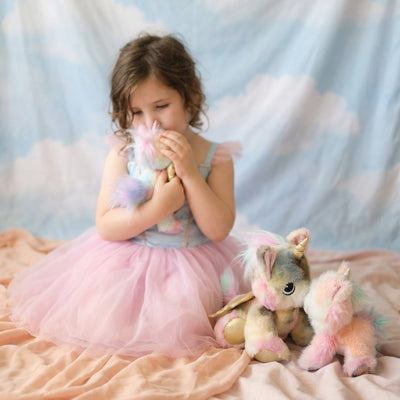 Dinkum Caticorn - Tinx soft rainbow plush toy cuddled by a child beside two pastel caticorn toys on a bed from Dinkum Pets