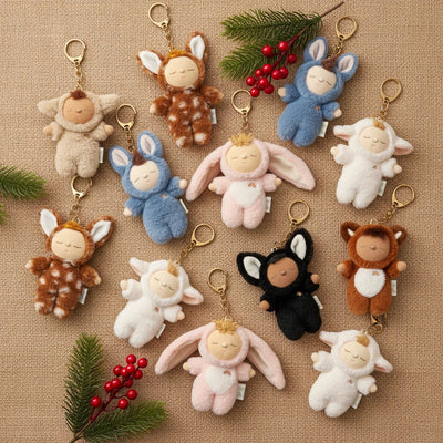 Cozy Bag Charm - Cat Nox black cat plush key chain with embroidered details and gold clip surrounded by soft animal bag charms on a festive backdrop