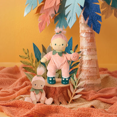 Dream Dinkum Doll Piper Peach by Dinkum Dolls by Olli Ella in a peach outfit holding a peach fruit beside a smaller soft doll in a colourful jungle scene