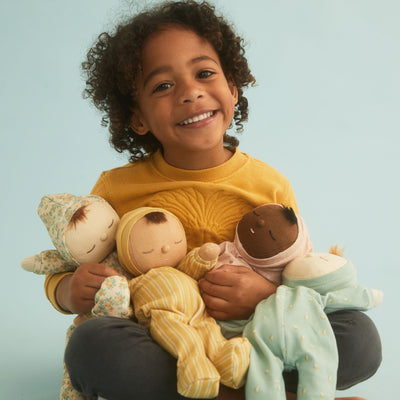 Dozy Dinkum Pickle Blossom soft doll held by a smiling child alongside three other soft dolls in colourful outfits from Dinkum Dolls by Olli Ella