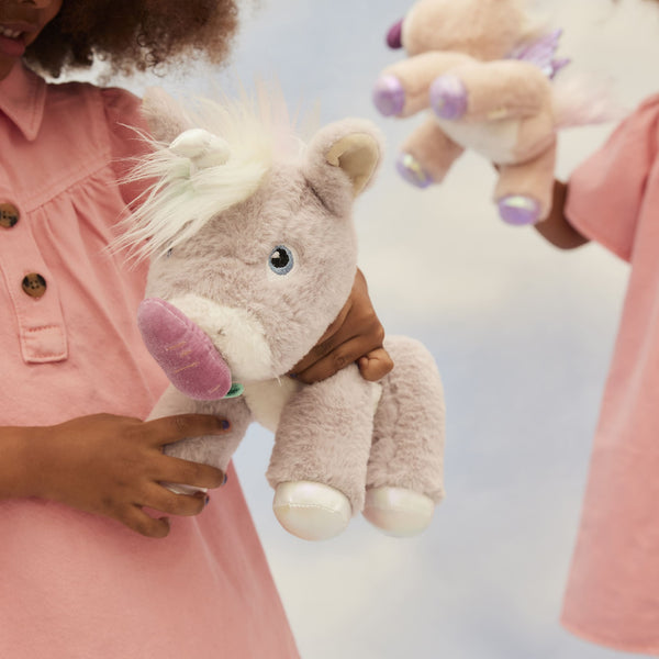 Dinkum Unicorn - Glimmer by Dinkum Unicorns is a soft lilac plush unicorn toy held by a child with another unicorn friend in the background