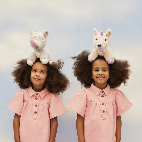 Dinkum Unicorn - Glimmer by Dinkum Unicorns perched on the heads of two smiling children showcasing a soft lilac plush unicorn toy for imaginative play