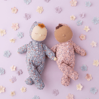 Dozy Dinkum - Tootsie Briar soft doll in a floral romper beside a second floral doll on a lavender background with scattered fabric flowers