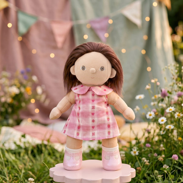 Doll in a pink dress standing on a small platform with flowers and flags in the background