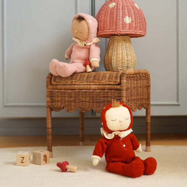 Dozy Dinkums - Toadstool Moppet soft red doll in a mushroom cap hood sits beside a wicker mushroom lamp and wooden toys in a cozy nursery scene