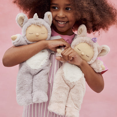 Cozy Dinkums - Unicorn - Sweetpea by Dozy Dinkums with a child cuddling two soft unicorn dolls in lavender and pink with wings and horns