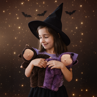 Cozy Dinkum - Bat Pip soft doll held by a child in a witch costume alongside another plush doll in a starry Halloween scene from Cozy Dinkums