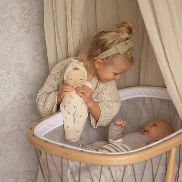 Lullaby Dozy Dinkum - Lyra soft doll held by a child beside a baby in a wooden cot from Dozy Dinkums for gentle imaginative play