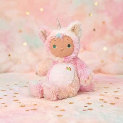 Plush toy in a pink unicorn costume on a soft, pastel background with lights.