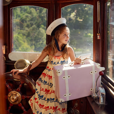 See-Ya Suitcase - Sorbet by Olli Ella Kids in soft pink held by a child inside a vintage train carriage for playful travel adventures