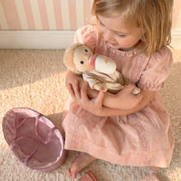 Young girl in a pink dress holding a teddy bear on a carpeted floor.
