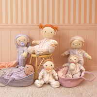 Collection of baby dolls and toys in a nursery setting with striped wallpaper.