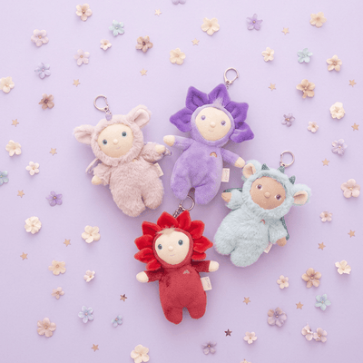 Four colorful plush keychains on a light purple background with flowers.