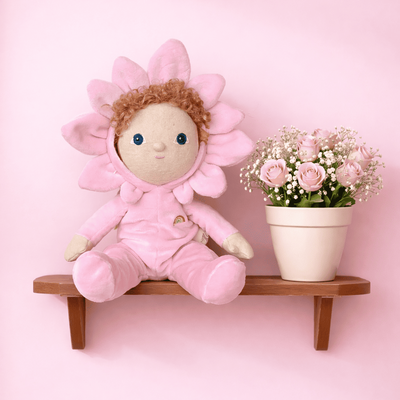 Pink plush flower-shaped toy on a wooden shelf with a pink background