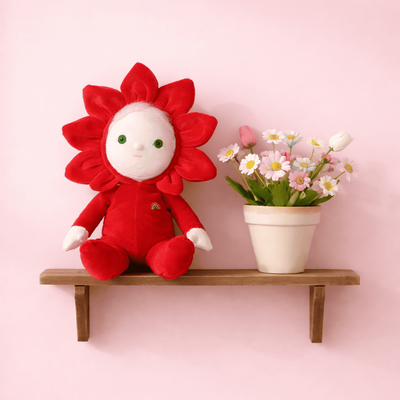 Red flower-shaped plush toy on a wooden shelf with a pink background