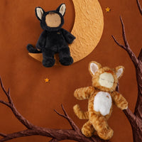 Two plush cat toys posed against a warm brown backdrop: one black cat sitting on a crescent moon and one orange tabby cat perched on a tree branch. Small gold stars decorate the scene.
