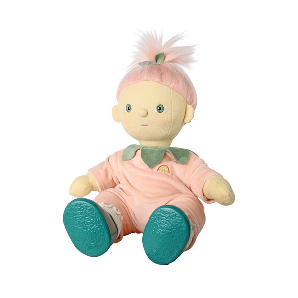 A soft plush baby doll with pale yellow skin, pink hair in a small ponytail with a green bow, wearing a pink outfit with a green collar and teal shoes, shown on a plain white background.