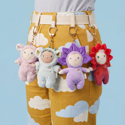 Person wearing mustard yellow pants with cloud patterns, holding four colorful plush keychains.