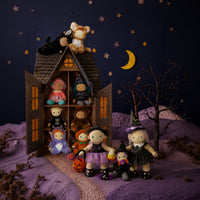 A styled collection of handmade plush dolls arranged around a miniature haunted house diorama at night. The dolls wear various Halloween costumes, including witch, pumpkin, and animal themes, set against a dark blue starry sky backdrop with a crescent moon.