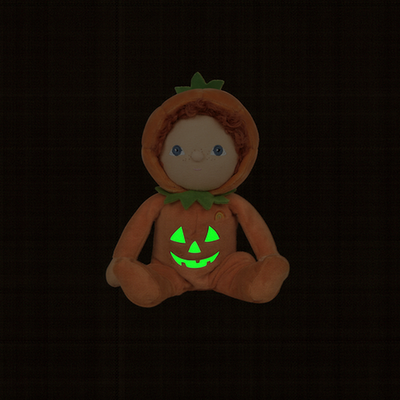 Plush toy in a pumpkin costume with glowing green face on a black background