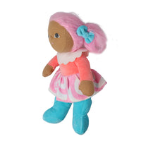 A soft plush doll with brown fabric skin, pink yarn hair tied with a blue bow, wearing a pink and white patterned dress, coral top, and blue shoes, isolated on a white background.