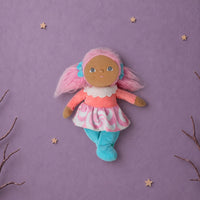A handmade fabric doll with pink hair, a brown face, and a pink and white dress, floating against a purple background decorated with stars, clouds, and branches.