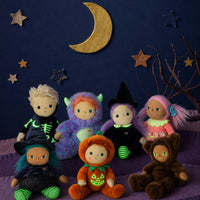 A group of seven plush Halloween dolls dressed in various costumes, arranged on a purple surface against a dark blue background decorated with a gold crescent moon and wooden stars.