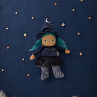 A witch doll with teal hair, wearing a dark blue pointed hat with a silver crescent moon, a dark blue dress, and striped socks, floating against a dark blue starry background with white clouds at the bottom.