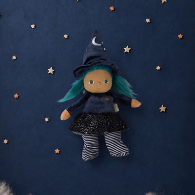 A witch doll with teal hair, wearing a dark blue pointed hat with a silver crescent moon, a dark blue dress, and striped socks, floating against a dark blue starry background with white clouds at the bottom.