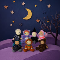 Six plush dolls dressed in Halloween costumes are arranged on a purple felt landscape with a dark blue sky backdrop, gold stars, a crescent moon, and a bare tree.