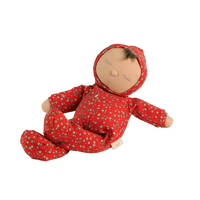Soft baby doll with sleepy embroidered closed eyes, a smiling mouth and a tuft of dark brown hair, wearing a red footed sleepsuit and matching bonnet with a ditsy floral print, button placket, and a small embroidered rainbow.
