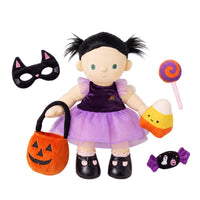 A Halloween-themed plush doll with black pigtails, a purple dress, and a lavender skirt, shown with matching accessories including an orange pumpkin bucket, black cat mask, candy corn, lollipop, and ghost candy on a white background.