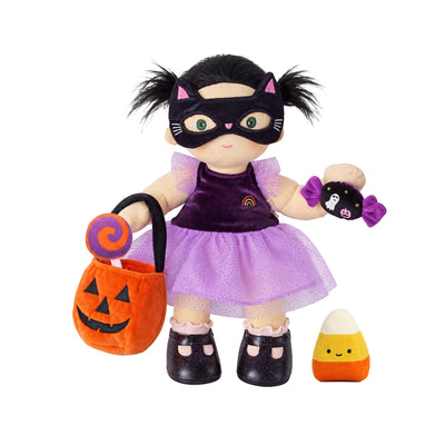 A Halloween-themed doll dressed in a black cat mask and purple dress, holding an orange pumpkin bucket with a lollipop and a small purple spider plush, with a candy corn accessory beside it, on a white background.