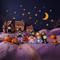 A Halloween-themed miniature diorama scene featuring small plush dolls in costumes, jack-o'-lanterns, toy houses, bare trees, and a crescent moon against a dark blue night sky with paper stars.