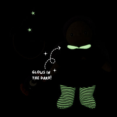 A dark doll or toy figure wearing glow-in-the-dark striped socks and a glowing green bow tie, with stars and the text 'GLOWS IN THE DARK!' on a black background.