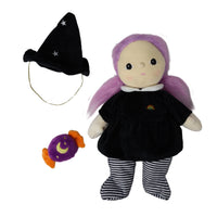 A witch-themed plush doll with long purple hair, wearing a black dress and black-and-white striped socks, shown with a black pointed hat and a small purple and orange crescent moon accessory on a plain white background.