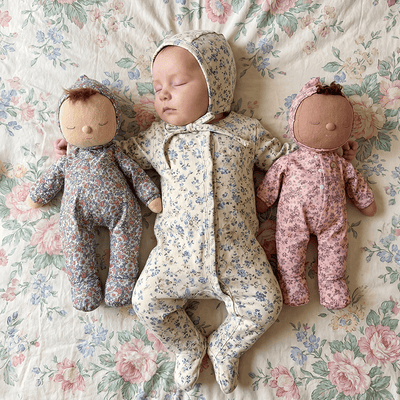 Baby in floral outfit with two dolls on a floral-patterned surface