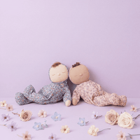 Two soft toys sitting on a light purple surface with flowers around them.