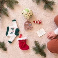 Christmas doll accessory set: a cream knit jumper with green trim and an embroidered rainbow and holly design, a red plush stocking with white fluffy cuff, a red and white striped plush candy cane, a holly-print gift box with a green velvet bow, and a felt “To Santa, The North Pole” letter.