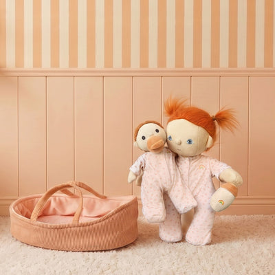 Two plush toys with red hair and a pink basket on a beige carpet with striped wall.