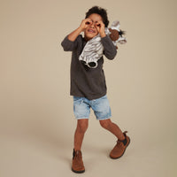 Cozy Dinkums - Zebra Mini soft zebra doll cuddled by a smiling child in a playful studio portrait with denim shorts and boots