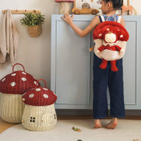 Dozy Dinkums - Toadstool Moppet soft doll carried in a red spotted toadstool backpack by a child in a cosy playroom