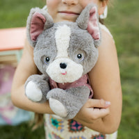 Dinkum Dogs - Gizmo grey plush dog with white markings and a pink collar held by a smiling child outdoors for cuddly imaginative play
