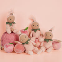 Dinky Dinkums Fruity Cuties - Peggy Peach soft doll pictured with three matching dolls and fresh peaches on a pink background