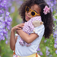 Dozy Dinkums - Twinkle Plum Check soft doll cuddled by a smiling child in a flower garden wearing a plum and white check outfit