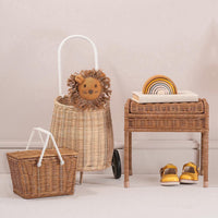 Piki Rattan Basket - Natural woven children's basket with a white carry handle beside a lion basket and rattan furniture with rainbow toy and shoes