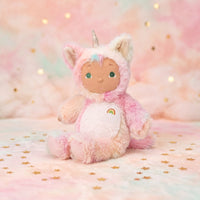 Plush toy in a pink unicorn costume on a soft, pastel background with lights.